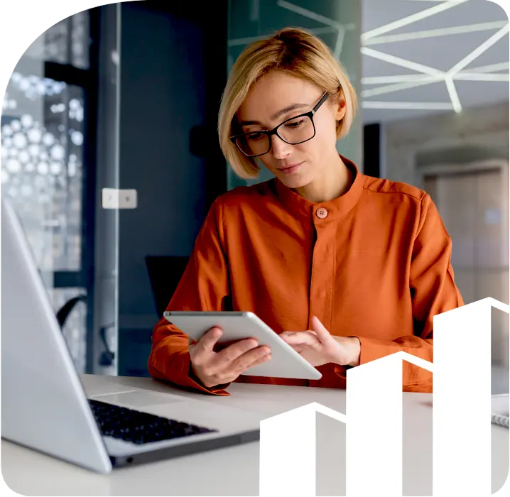 A business woman sitting at a desk in front of a laptop with a tablet.